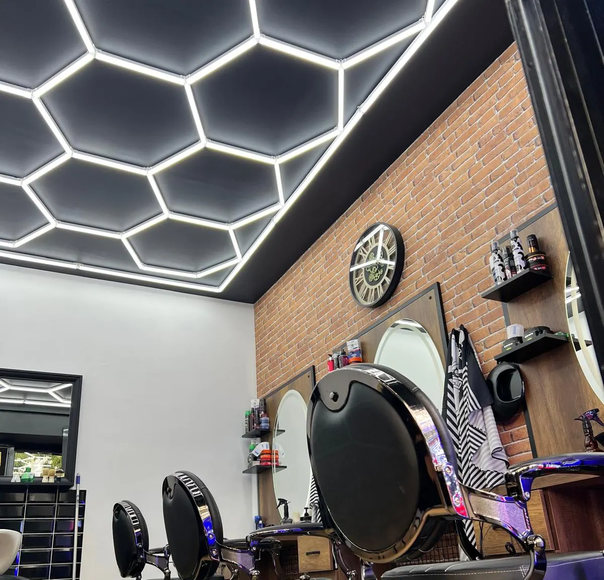 Le salon BEN Coiffure : plafond lumineux en alvéoles hexagonales, fauteuils noirs et chromés, mur de brique