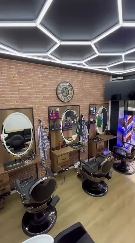 Vue d’ensemble du salon : trois postes, miroirs ronds éclairés, mur de brique